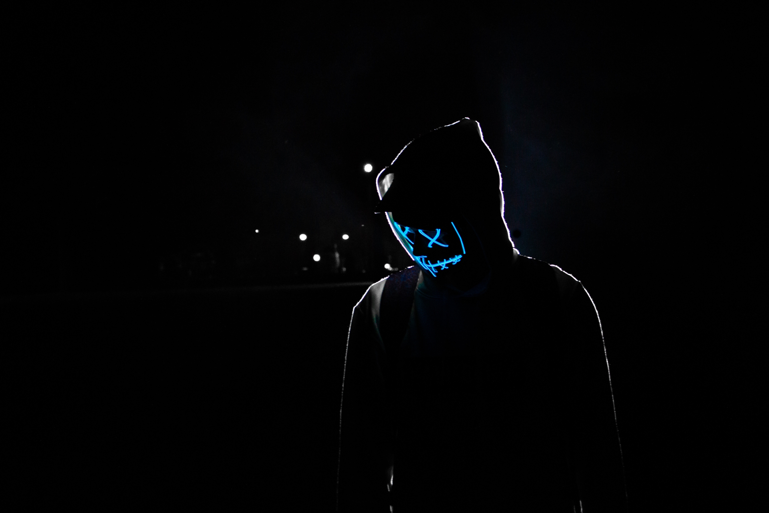 Person with neon mask resembling a stylized hacker at night
